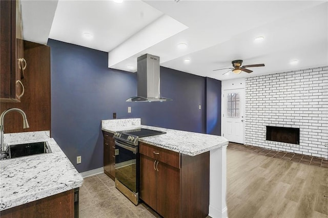 kitchen featuring stainless steel electric range oven, a peninsula, a sink, dark brown cabinetry, and wall chimney exhaust hood