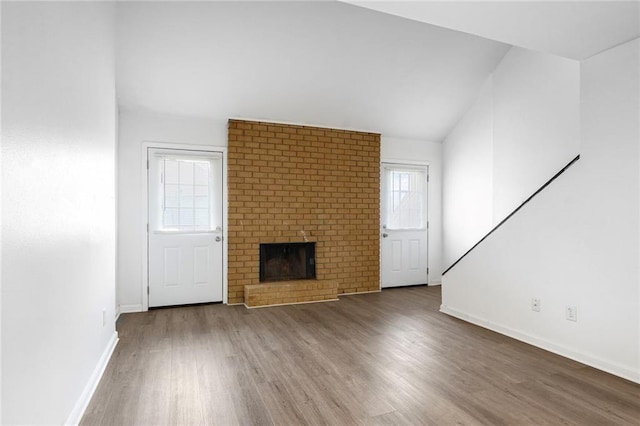 unfurnished living room with vaulted ceiling, a brick fireplace, wood finished floors, and baseboards