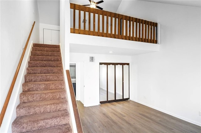 stairs featuring visible vents, wood finished floors, a high ceiling, baseboards, and ceiling fan