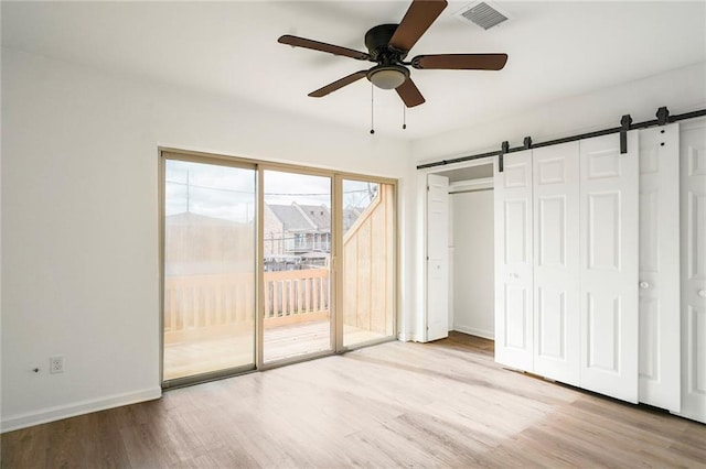 unfurnished bedroom featuring access to exterior, visible vents, a barn door, and wood finished floors