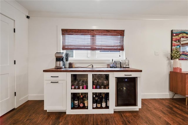 bar with dark wood-style floors, wine cooler, ornamental molding, a bar, and baseboards