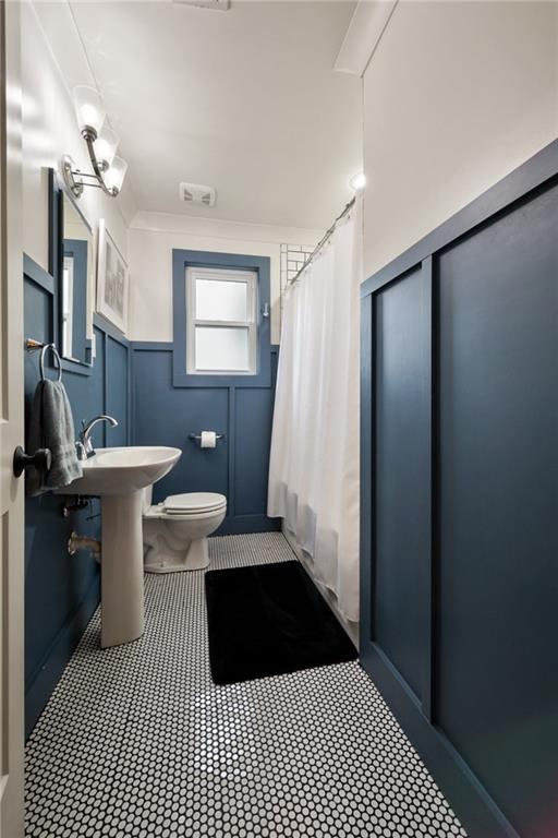 full bathroom featuring a shower with shower curtain, a decorative wall, and toilet