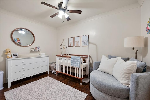 bedroom with dark wood-style floors, a nursery area, crown molding, and ceiling fan