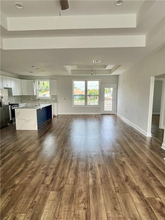 unfurnished living room featuring dark wood-style floors, a raised ceiling, visible vents, and baseboards