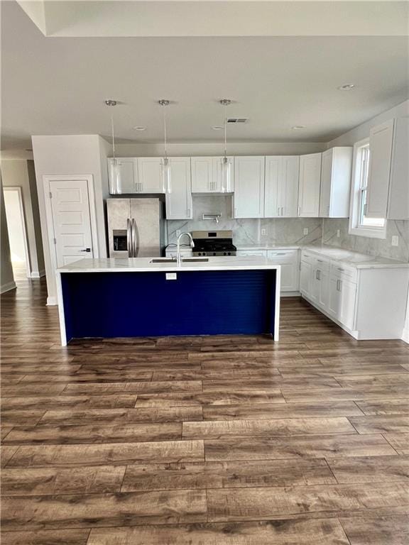 kitchen featuring stainless steel appliances, light countertops, dark wood-type flooring, a sink, and an island with sink