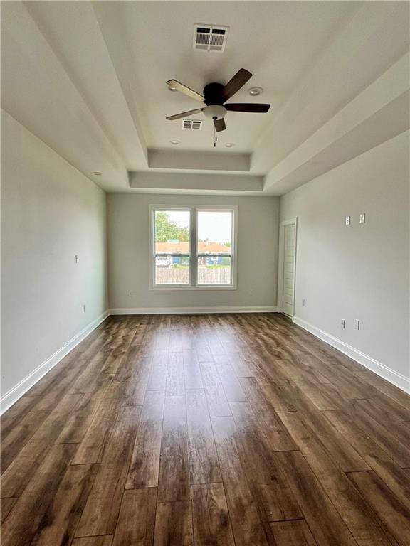 empty room featuring a tray ceiling, dark wood-style flooring, and visible vents