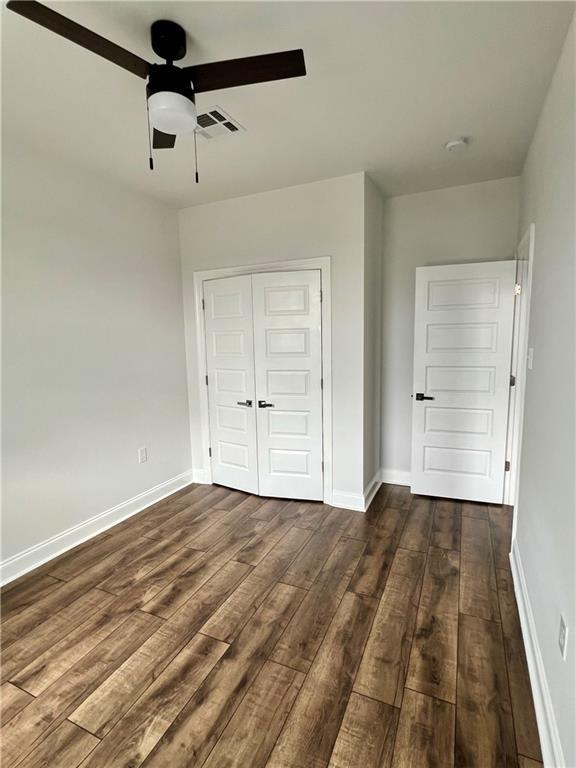 unfurnished bedroom with dark wood-type flooring, a closet, visible vents, and baseboards