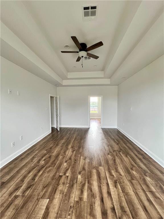 unfurnished room with visible vents, dark wood finished floors, baseboards, ceiling fan, and a tray ceiling