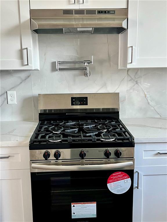 kitchen featuring white cabinets, light stone counters, stainless steel gas range, under cabinet range hood, and backsplash