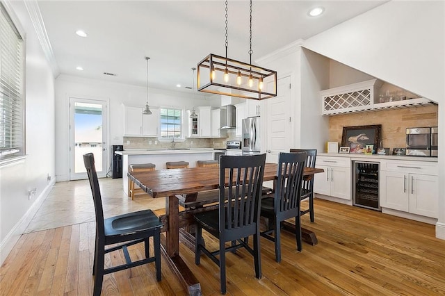 dining room featuring beverage cooler, ornamental molding, baseboards, and light wood-style floors