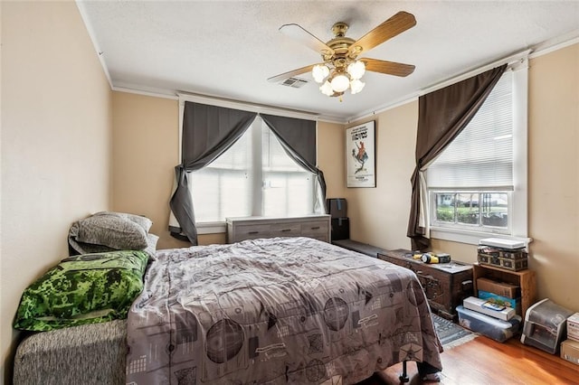 bedroom featuring visible vents, ceiling fan, wood finished floors, a textured ceiling, and crown molding