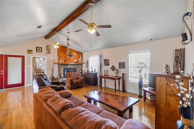 living area featuring lofted ceiling with beams, a fireplace, visible vents, a ceiling fan, and light wood-type flooring