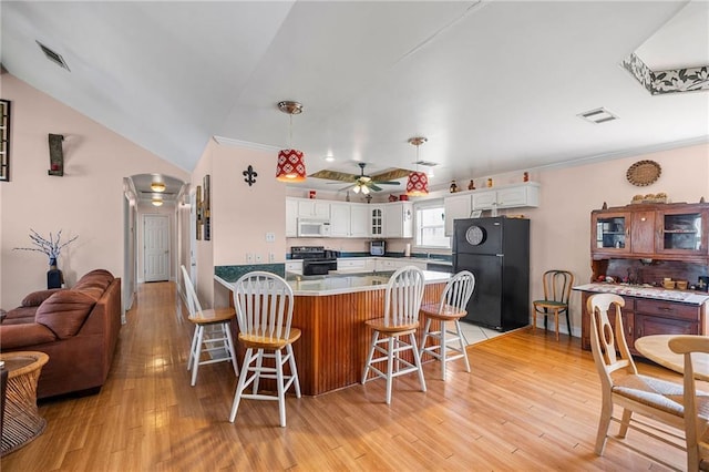 kitchen with electric range, white microwave, a breakfast bar area, freestanding refrigerator, and white cabinetry