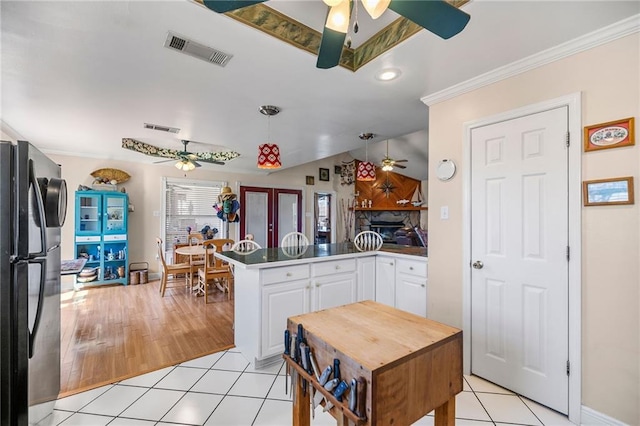 kitchen with light tile patterned floors, visible vents, white cabinets, freestanding refrigerator, and a peninsula