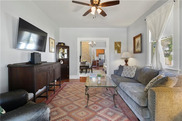 living area with ceiling fan with notable chandelier, wood finished floors, and baseboards