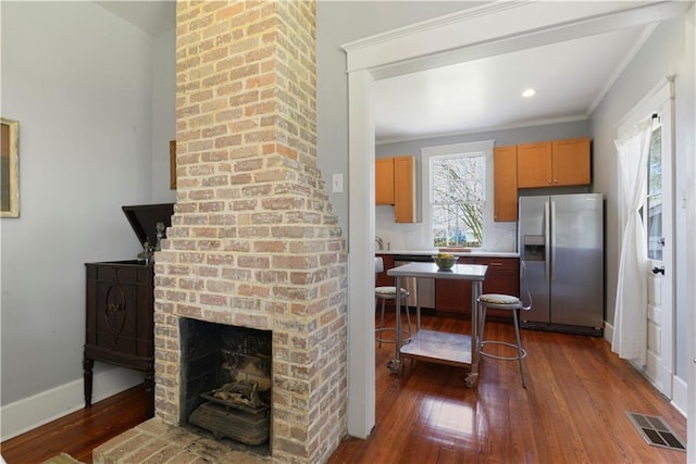 kitchen with visible vents, dark wood-type flooring, stainless steel appliances, crown molding, and a fireplace