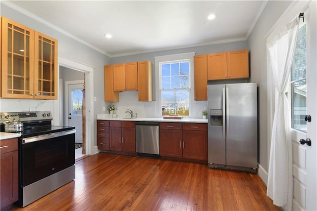 kitchen with appliances with stainless steel finishes, ornamental molding, dark wood-type flooring, light countertops, and a sink