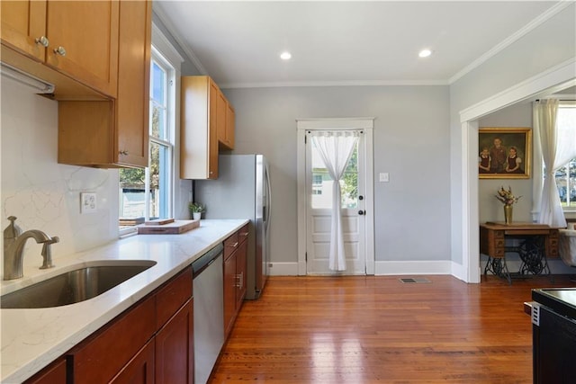 kitchen with crown molding, stainless steel dishwasher, a sink, wood finished floors, and plenty of natural light