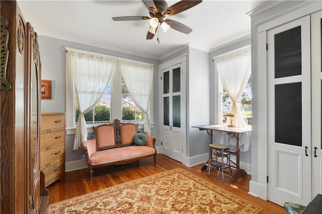 living area with ornamental molding, ceiling fan, baseboards, and wood finished floors