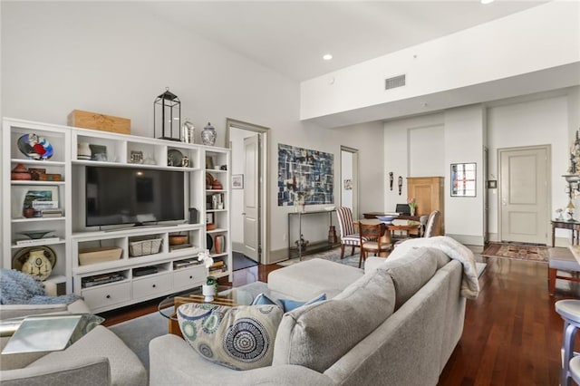 living area with a towering ceiling, baseboards, visible vents, and wood finished floors