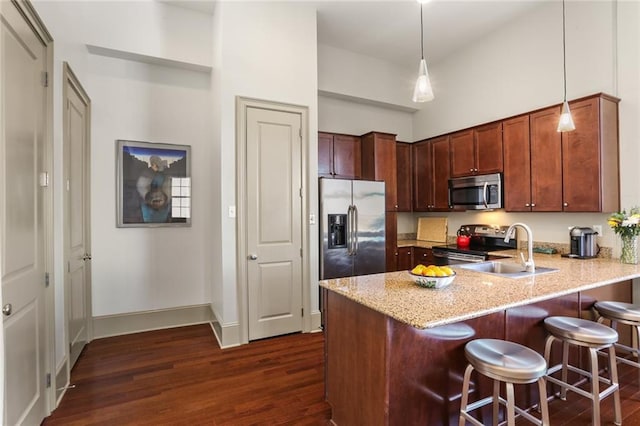 kitchen with dark wood-style floors, a breakfast bar area, appliances with stainless steel finishes, light stone countertops, and a peninsula