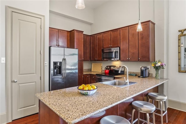 kitchen featuring a peninsula, hanging light fixtures, appliances with stainless steel finishes, light stone countertops, and dark wood finished floors