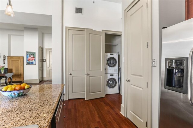 kitchen with light stone counters, visible vents, stainless steel refrigerator with ice dispenser, stacked washing maching and dryer, and dark wood-style floors