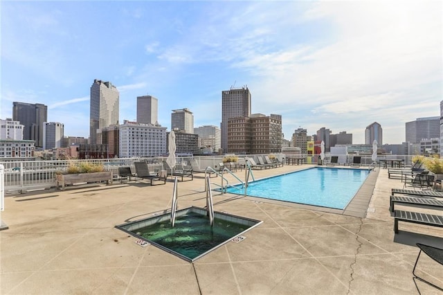 community pool with a view of city, a patio area, and a hot tub