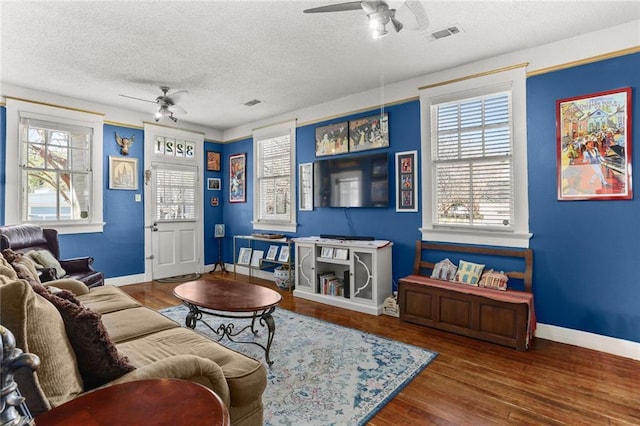 living room featuring a ceiling fan, visible vents, a textured ceiling, and wood finished floors