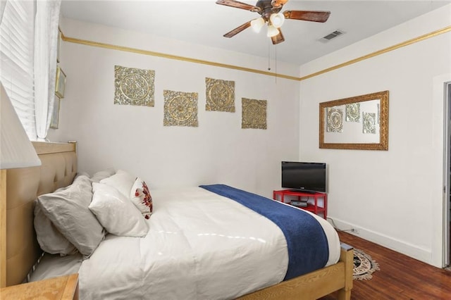 bedroom with a ceiling fan, visible vents, baseboards, and wood finished floors