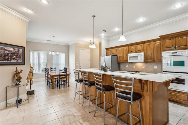 kitchen with brown cabinets, a breakfast bar area, light tile patterned floors, backsplash, and white appliances