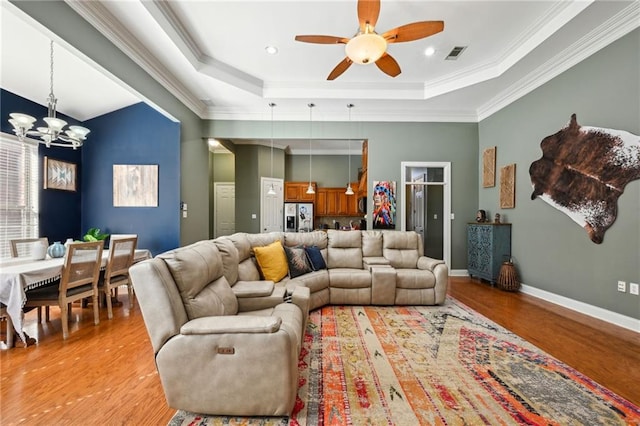 living room featuring a tray ceiling, visible vents, light wood-type flooring, baseboards, and ceiling fan with notable chandelier