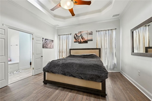 bedroom with a raised ceiling, crown molding, baseboards, and wood finished floors