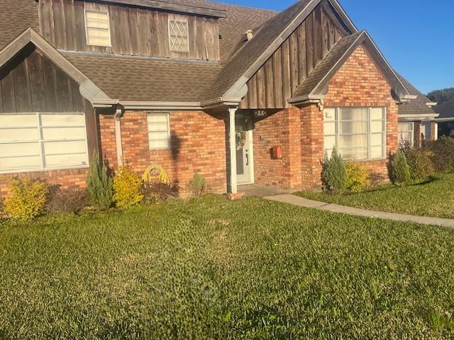 view of front of home with roof with shingles, a front yard, and brick siding