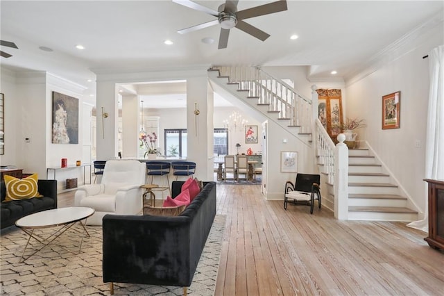 living area featuring hardwood / wood-style floors, baseboards, stairs, crown molding, and ceiling fan with notable chandelier