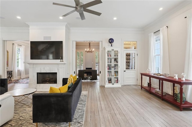 living area featuring recessed lighting, a fireplace, ornamental molding, ceiling fan with notable chandelier, and light wood-type flooring