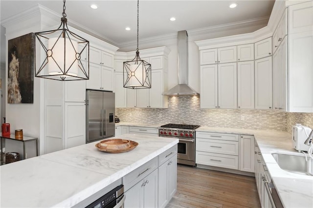 kitchen with light wood finished floors, stainless steel appliances, crown molding, wall chimney range hood, and tasteful backsplash