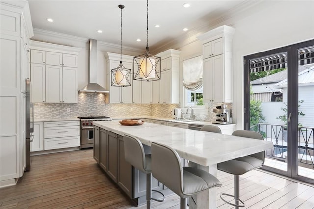 kitchen featuring high end stove, a sink, a center island, wall chimney range hood, and decorative backsplash