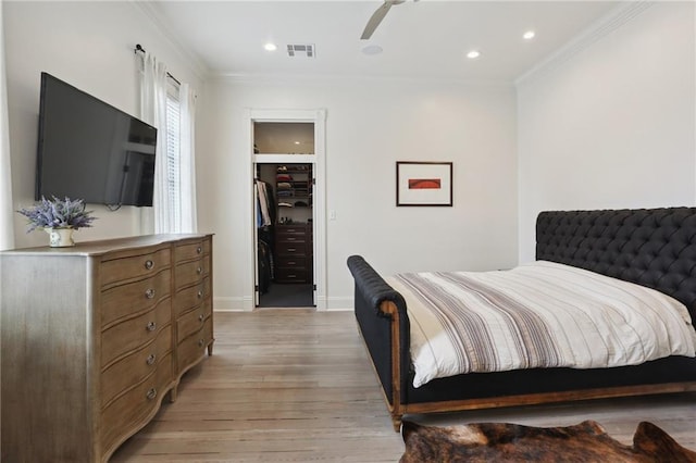 bedroom featuring visible vents, a walk in closet, light wood-style floors, and ornamental molding