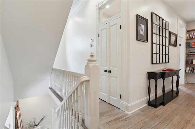 corridor with baseboards, an upstairs landing, and light wood-style flooring