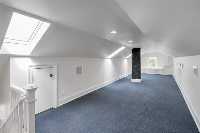 additional living space with baseboards, vaulted ceiling with skylight, visible vents, and dark carpet