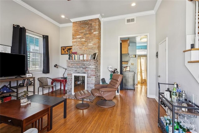 living area featuring crown molding, visible vents, a brick fireplace, baseboards, and hardwood / wood-style flooring