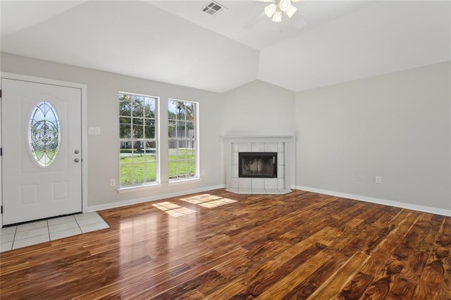 unfurnished living room with vaulted ceiling, light wood-type flooring, a tiled fireplace, and visible vents