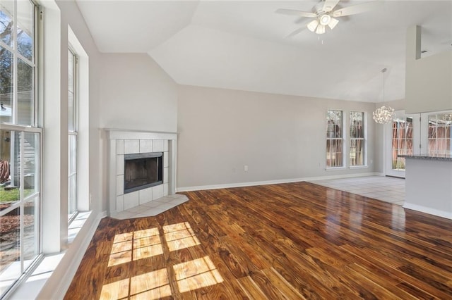 unfurnished living room with baseboards, vaulted ceiling, a tiled fireplace, and wood finished floors