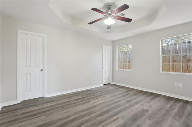 empty room with a tray ceiling, visible vents, baseboards, and wood finished floors