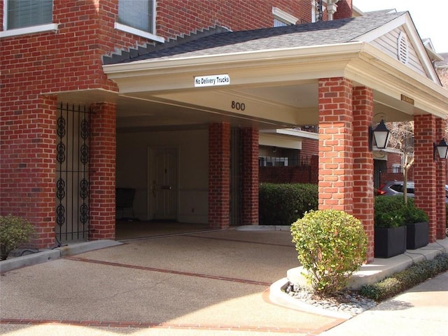 view of exterior entry with driveway, brick siding, and a shingled roof