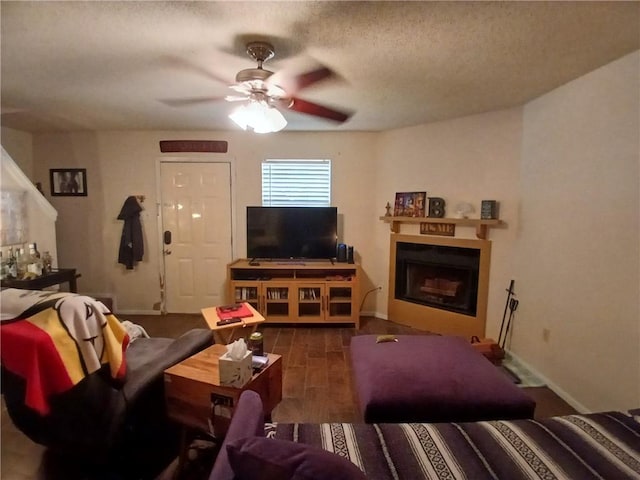 living room with a fireplace, a ceiling fan, a textured ceiling, wood finished floors, and baseboards