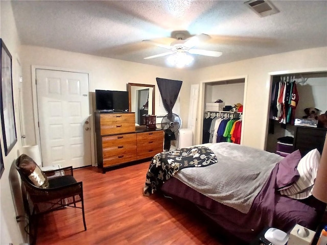 bedroom with multiple closets, visible vents, a ceiling fan, a textured ceiling, and wood finished floors