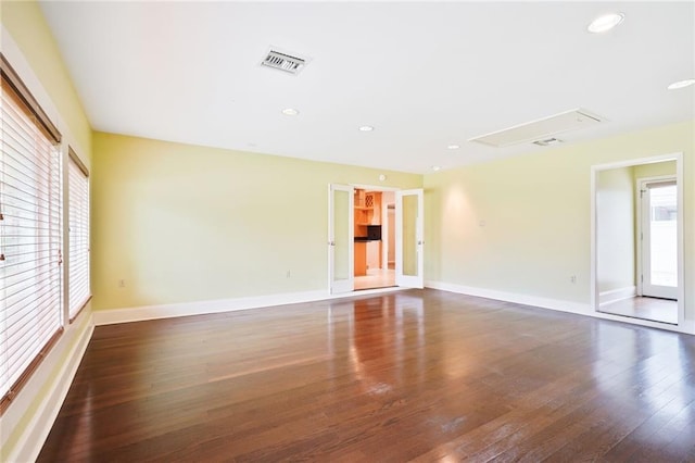 unfurnished room featuring baseboards, attic access, visible vents, and wood finished floors