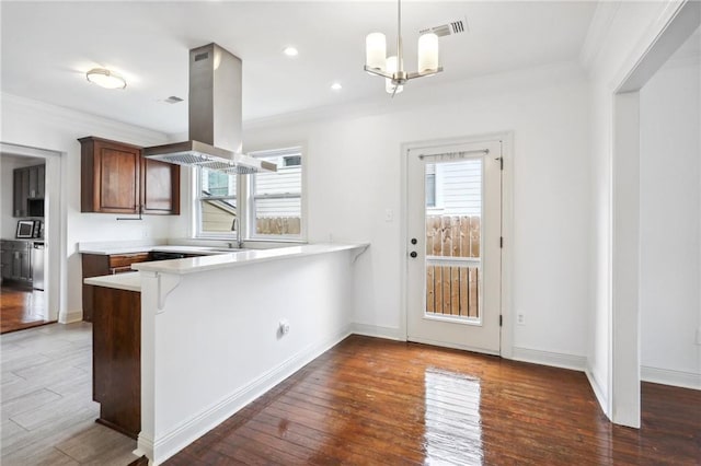 kitchen with a peninsula, wood-type flooring, island exhaust hood, and light countertops